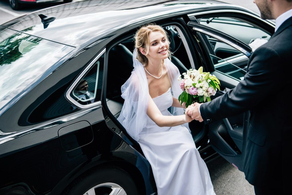 bridegroom in suit giving hand to attractive and smiling bride with bouquet