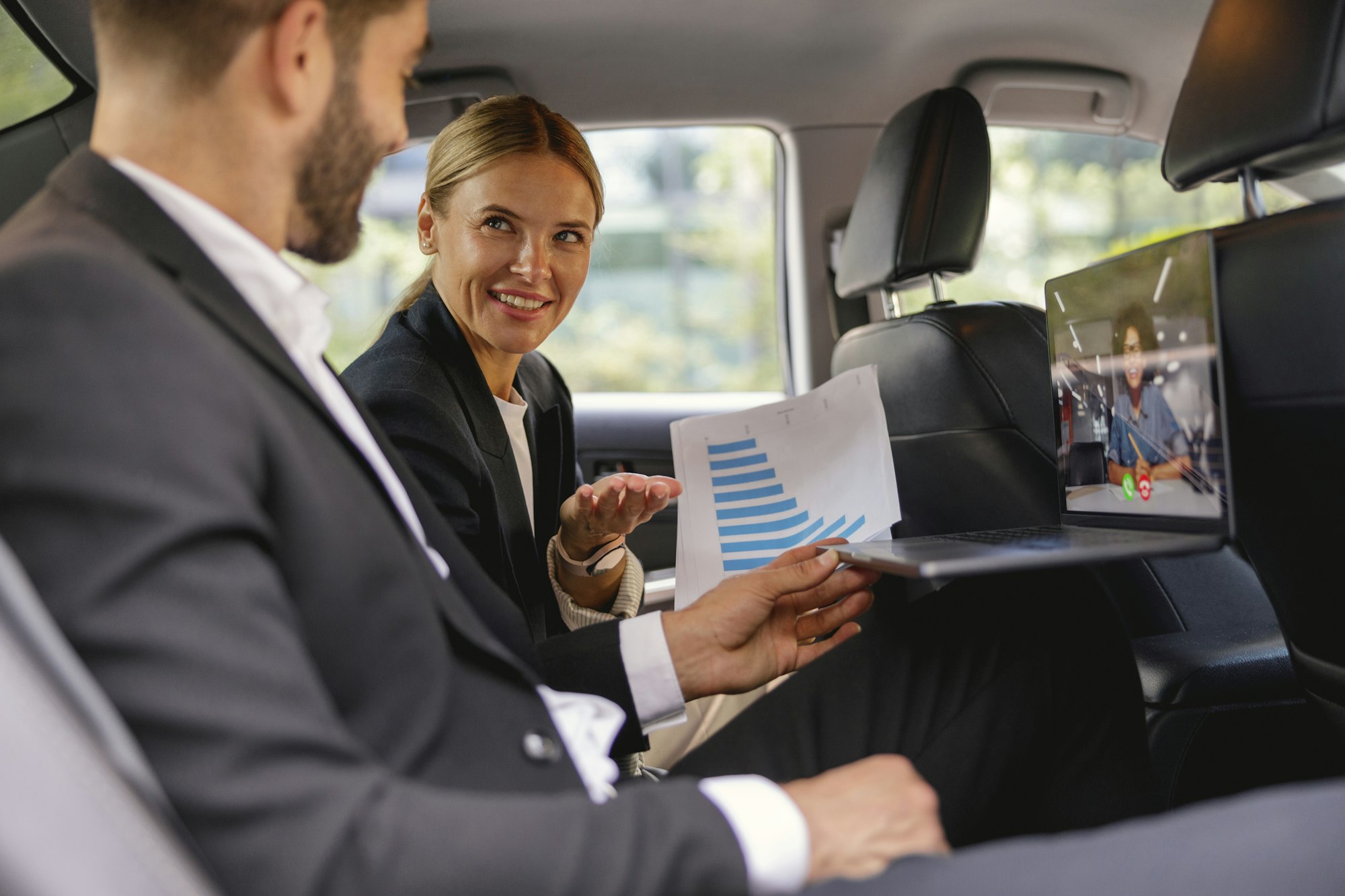 Business colleagues working with documents during video conference in back seat of car